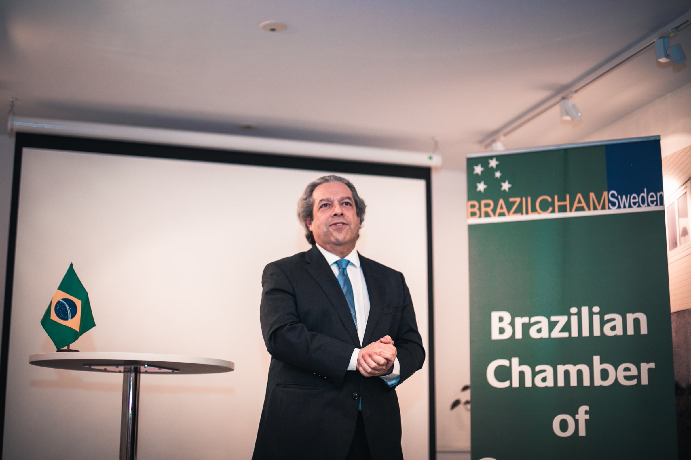 Speaker addressing the audience beside Brazilian and Swedish event details.