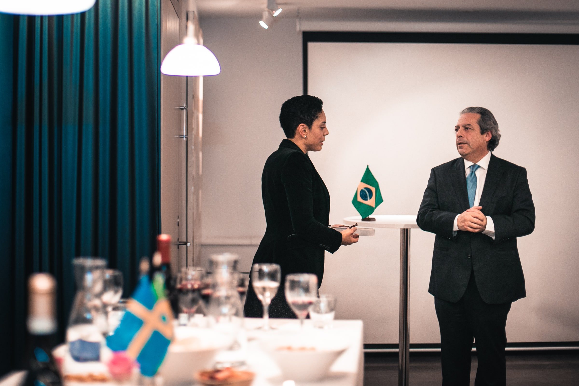 Two speakers exchanging remarks beside Brazilian and Swedish flags.