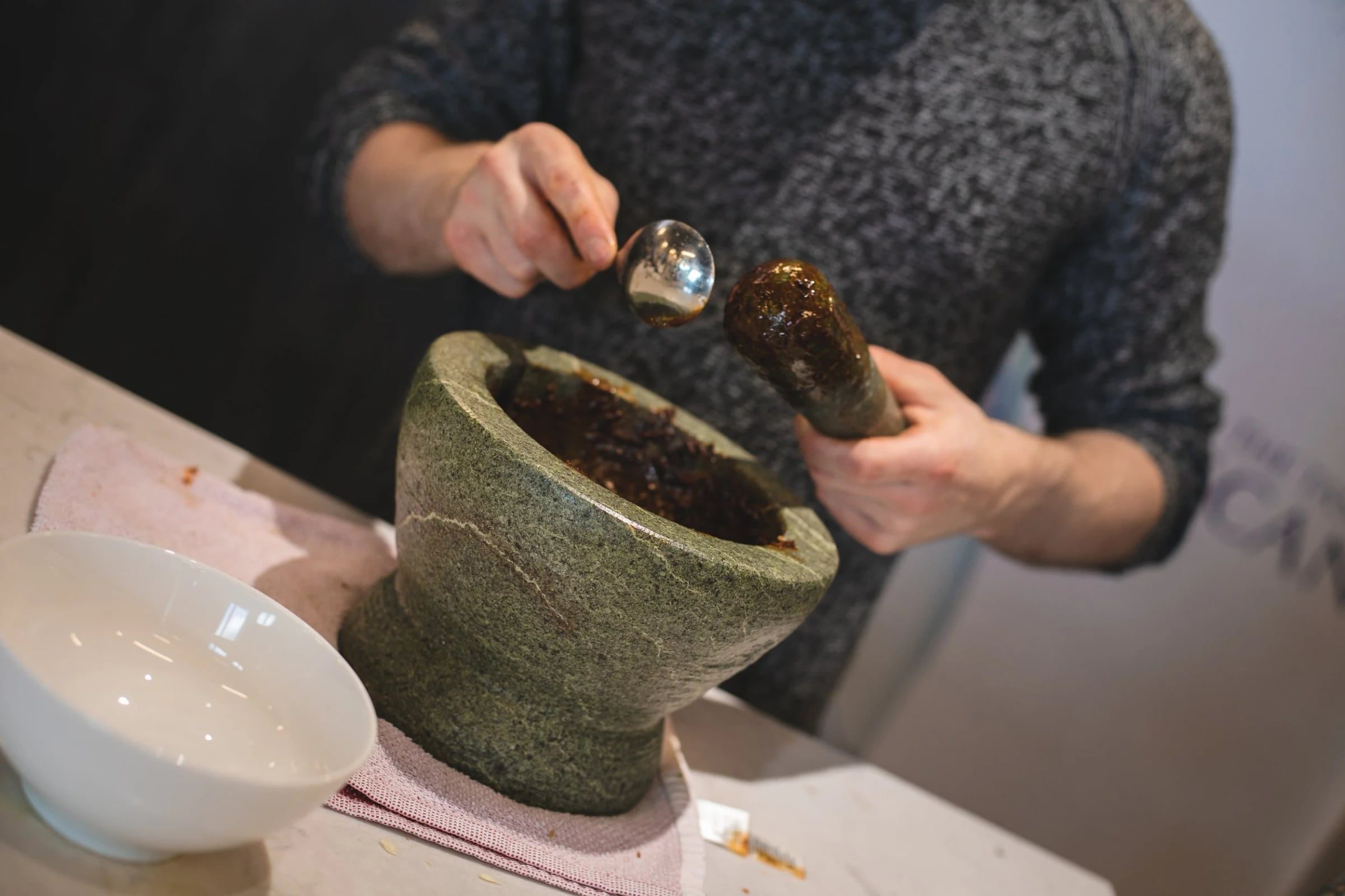 Participant grinding spices in a stone mortar during the cooking session