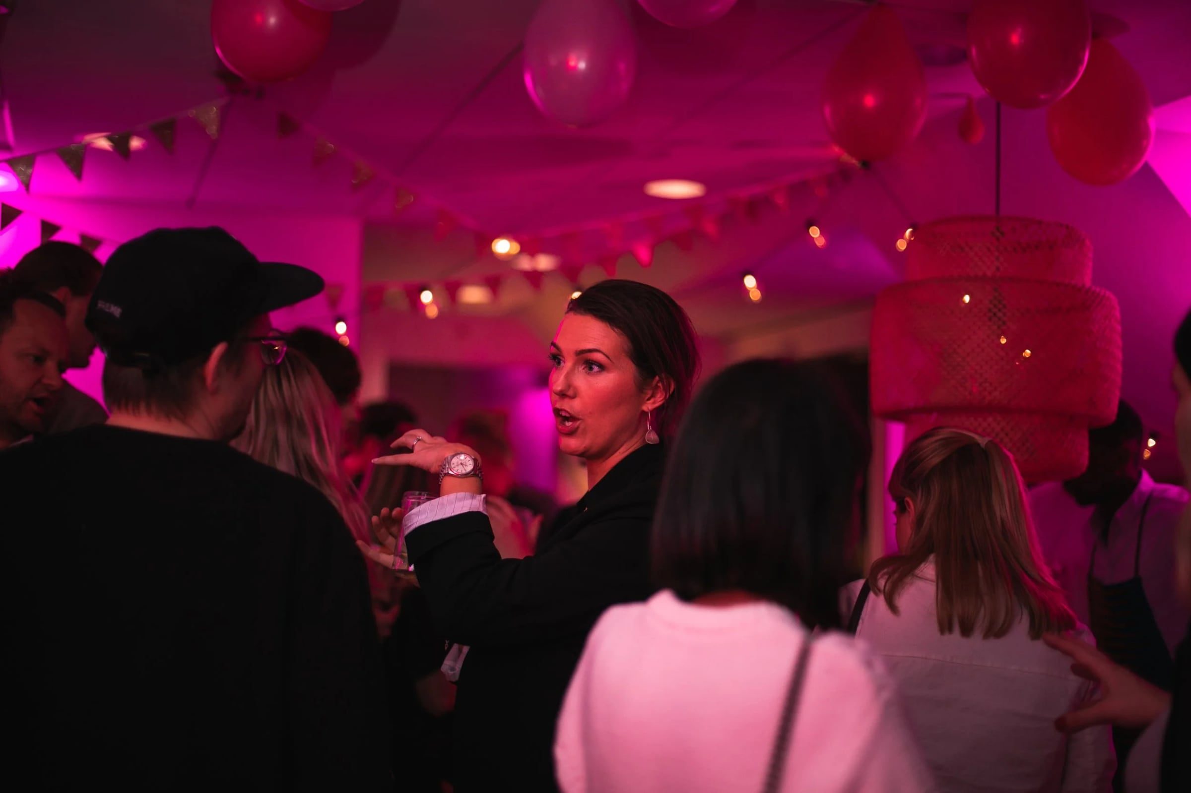 Guests talking at Relatable’s third-anniversary celebration under saturated pink light
