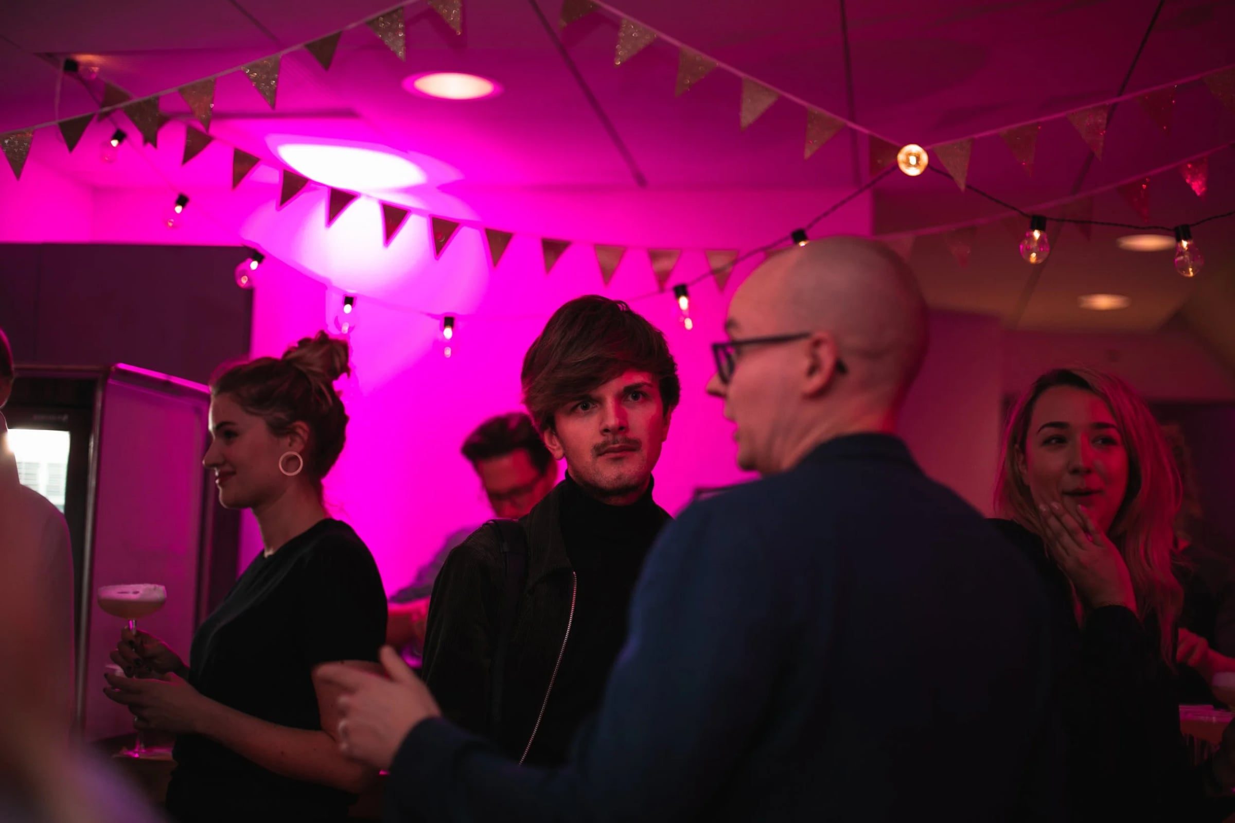 Guests networking across a busy pink-lit reception room