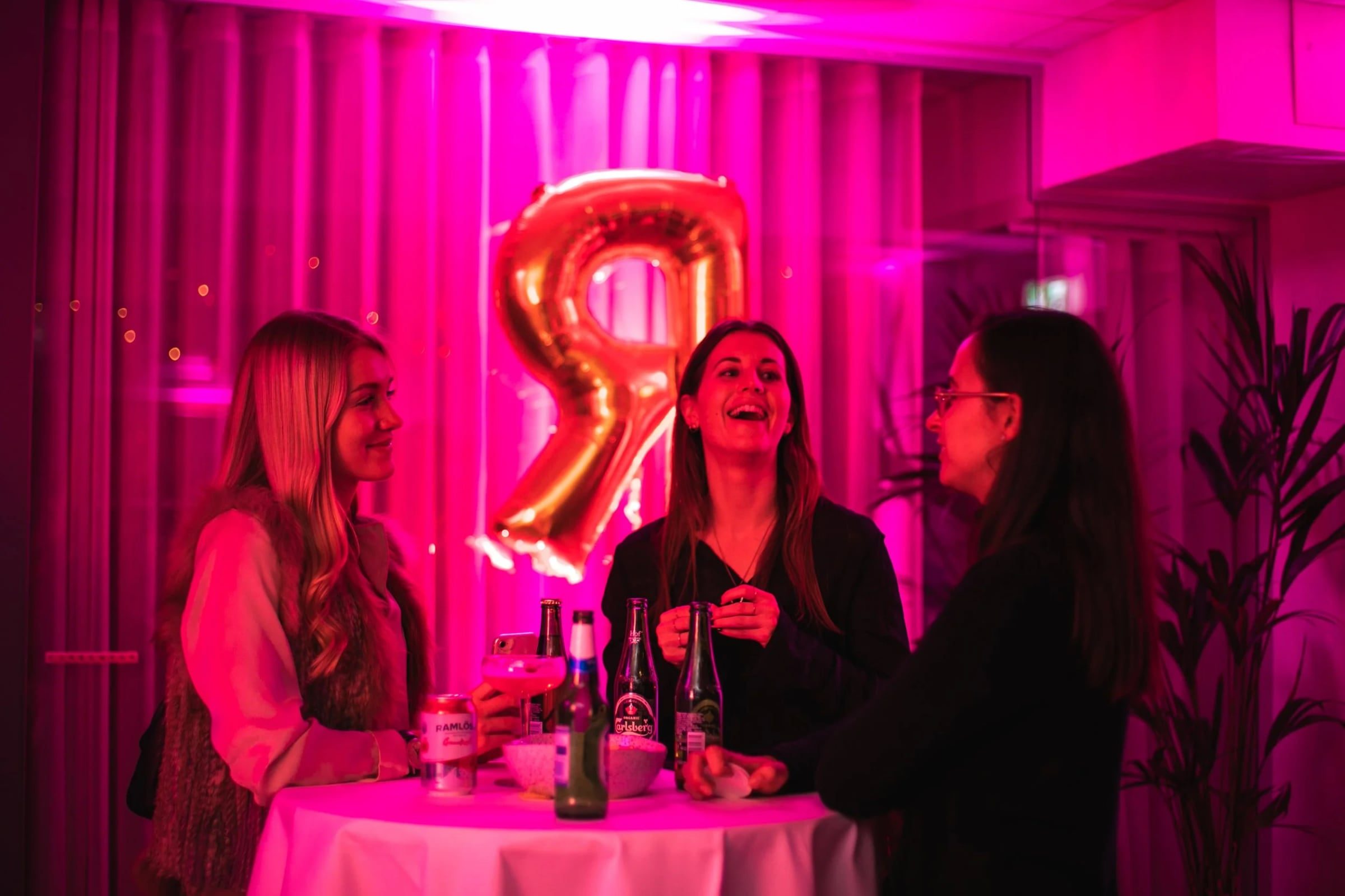Three women talking beside the gold event balloon
