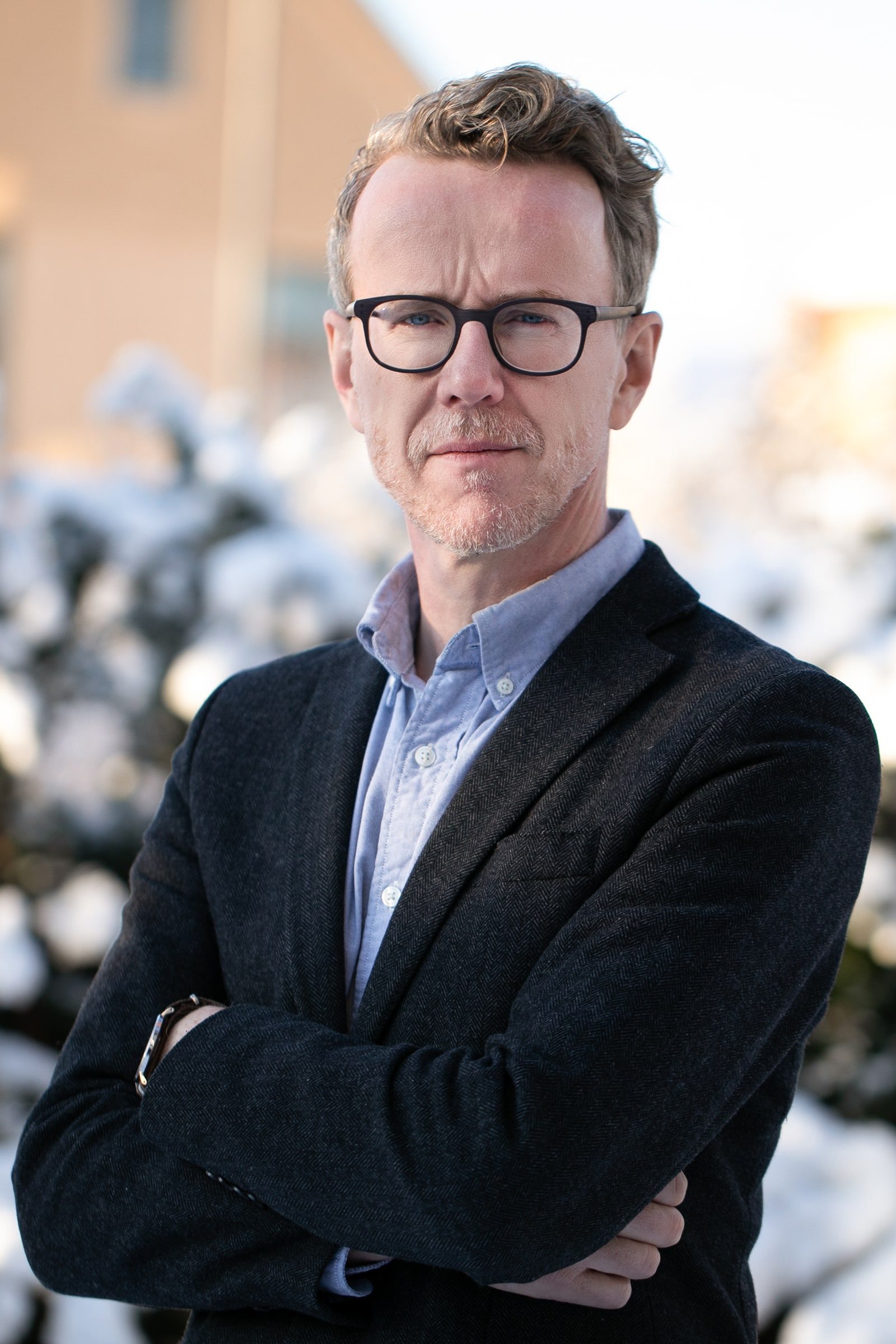 Professional outdoor portrait of a man in glasses, blue shirt and dark blazer.