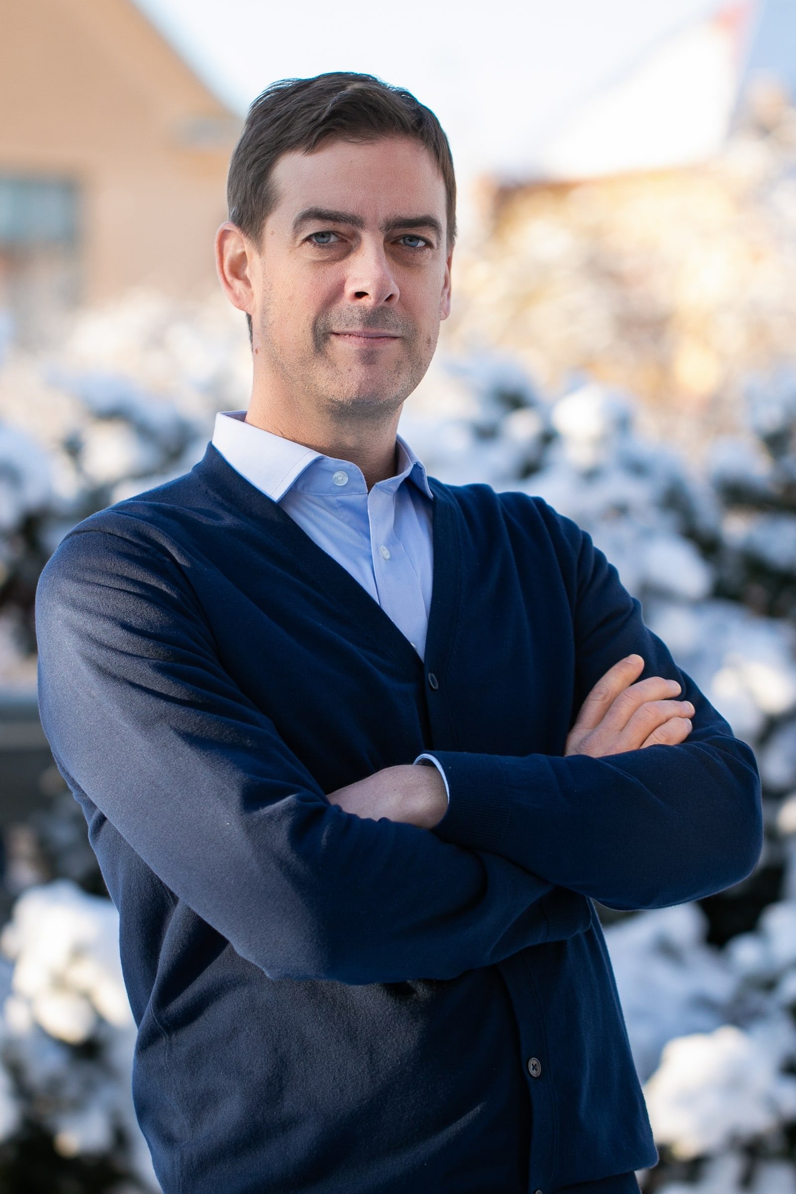 Close team portrait of a man in a navy sweater and pale blue shirt.