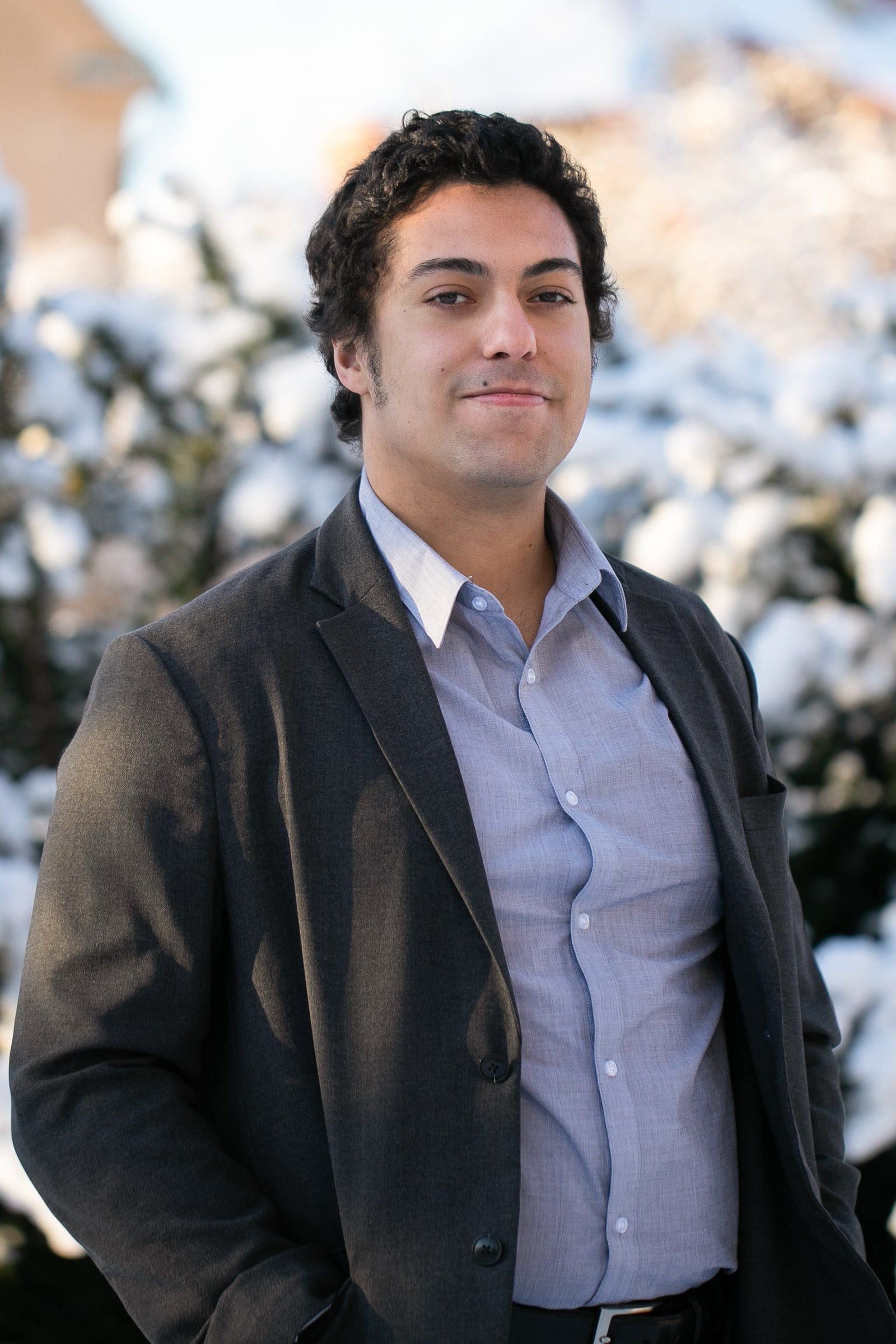 Close outdoor portrait of a man in a dark blazer and open-collar shirt.
