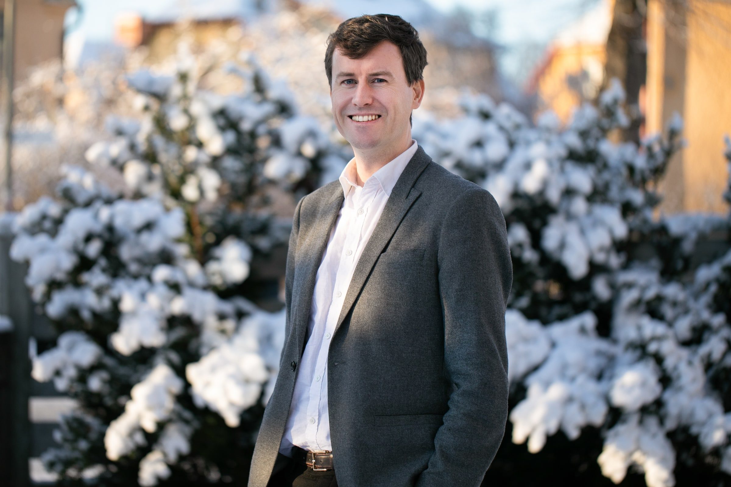 Team member in a grey blazer photographed standing against a snowy background.