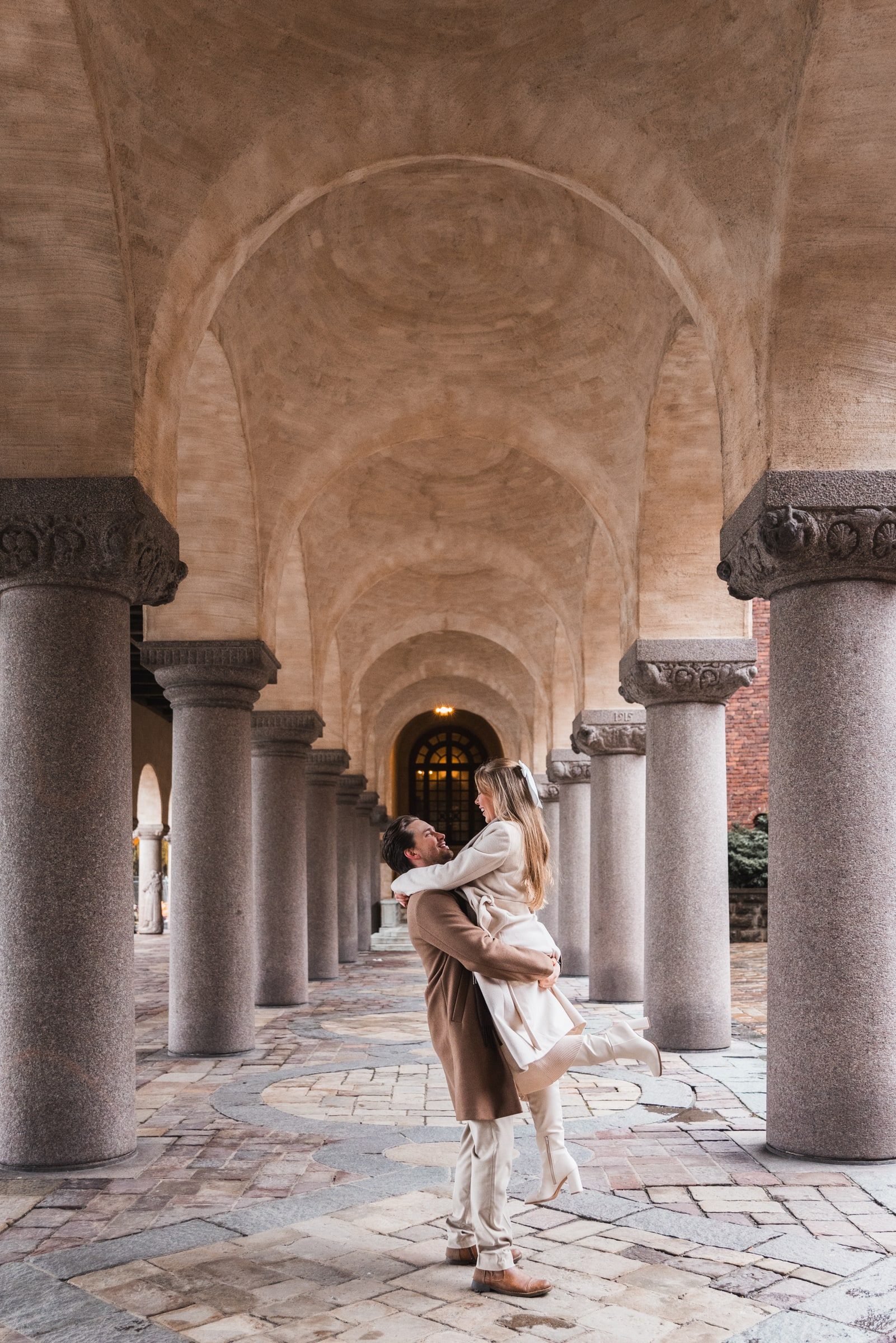 Couple embracing beneath stone arches during an engagement session.