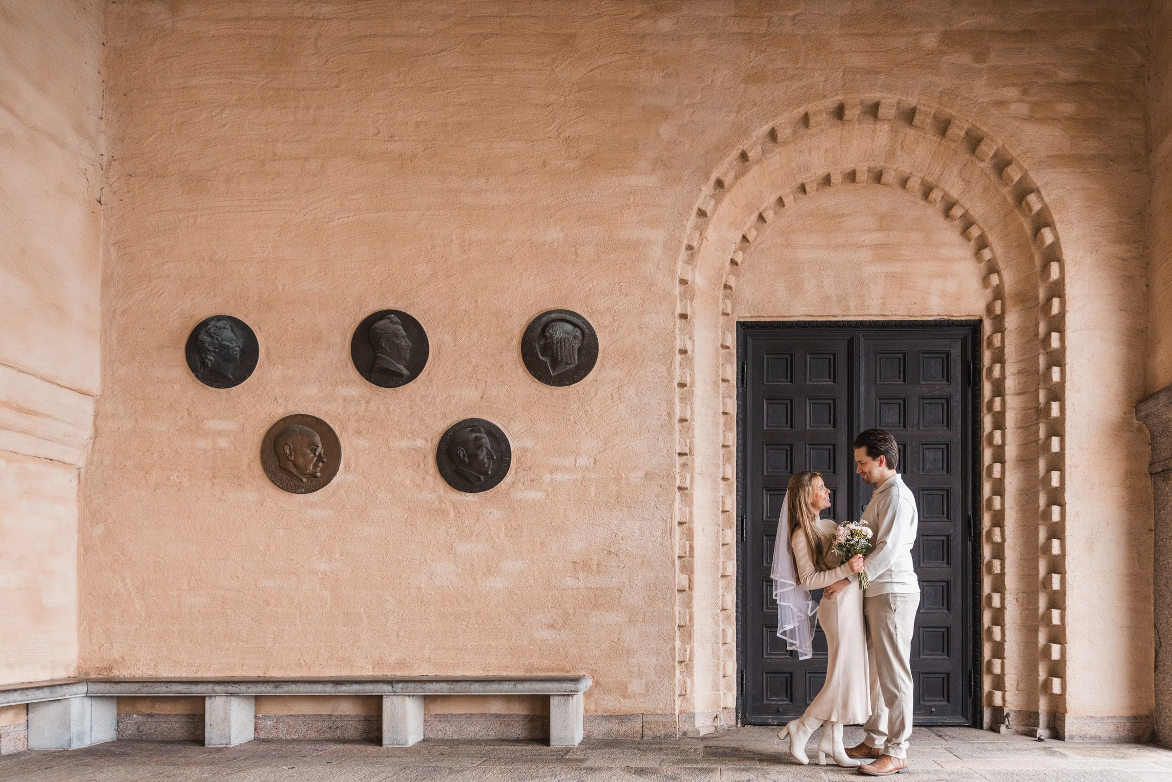 Wide engagement portrait framed by a warm textured wall and dark doorway.