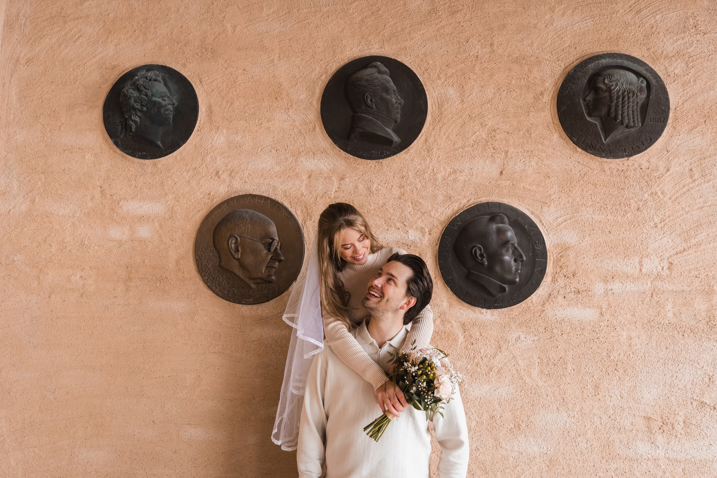 Playful couple portrait beneath a wall of sculpted medallions.