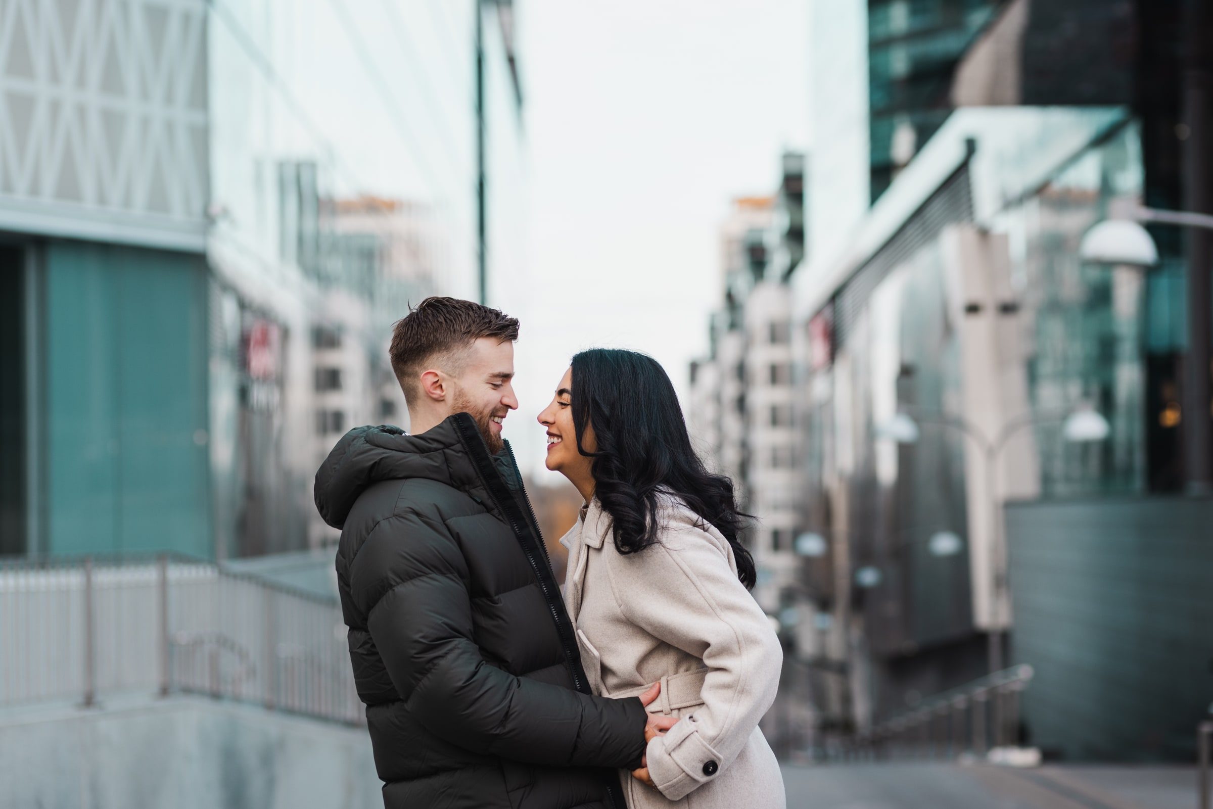 Couple laughing together among modern city buildings.
