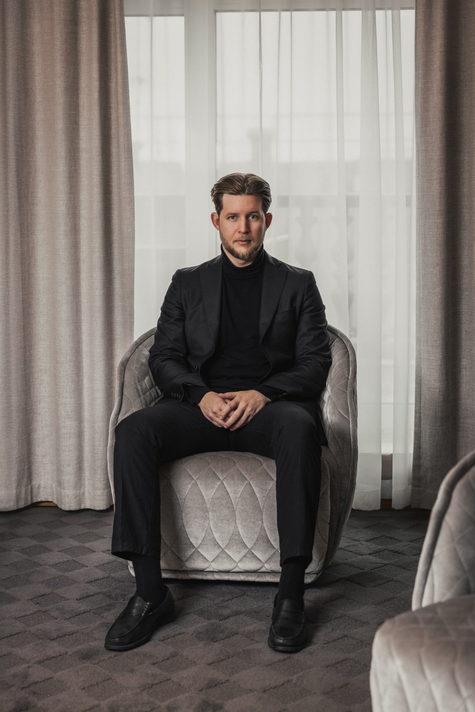 Concierge seated for a professional portrait beside a bright window.
