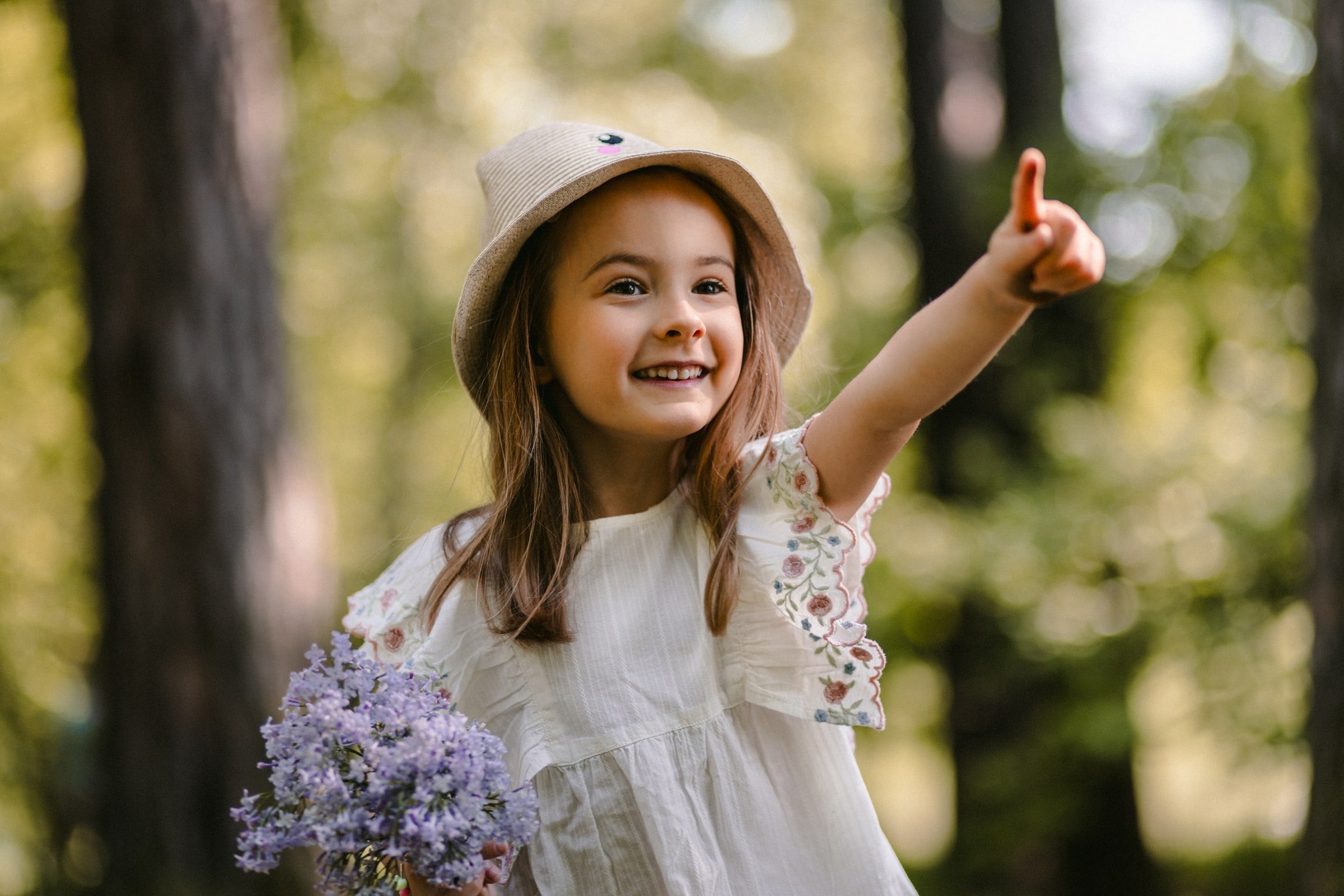 Young girl holding wildflowers and pointing through the sunlit trees.