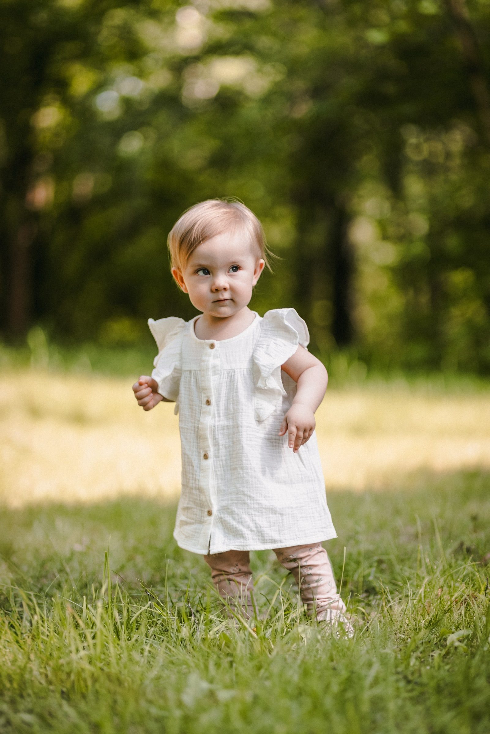 Toddler taking a few steps alone in a grassy woodland clearing.