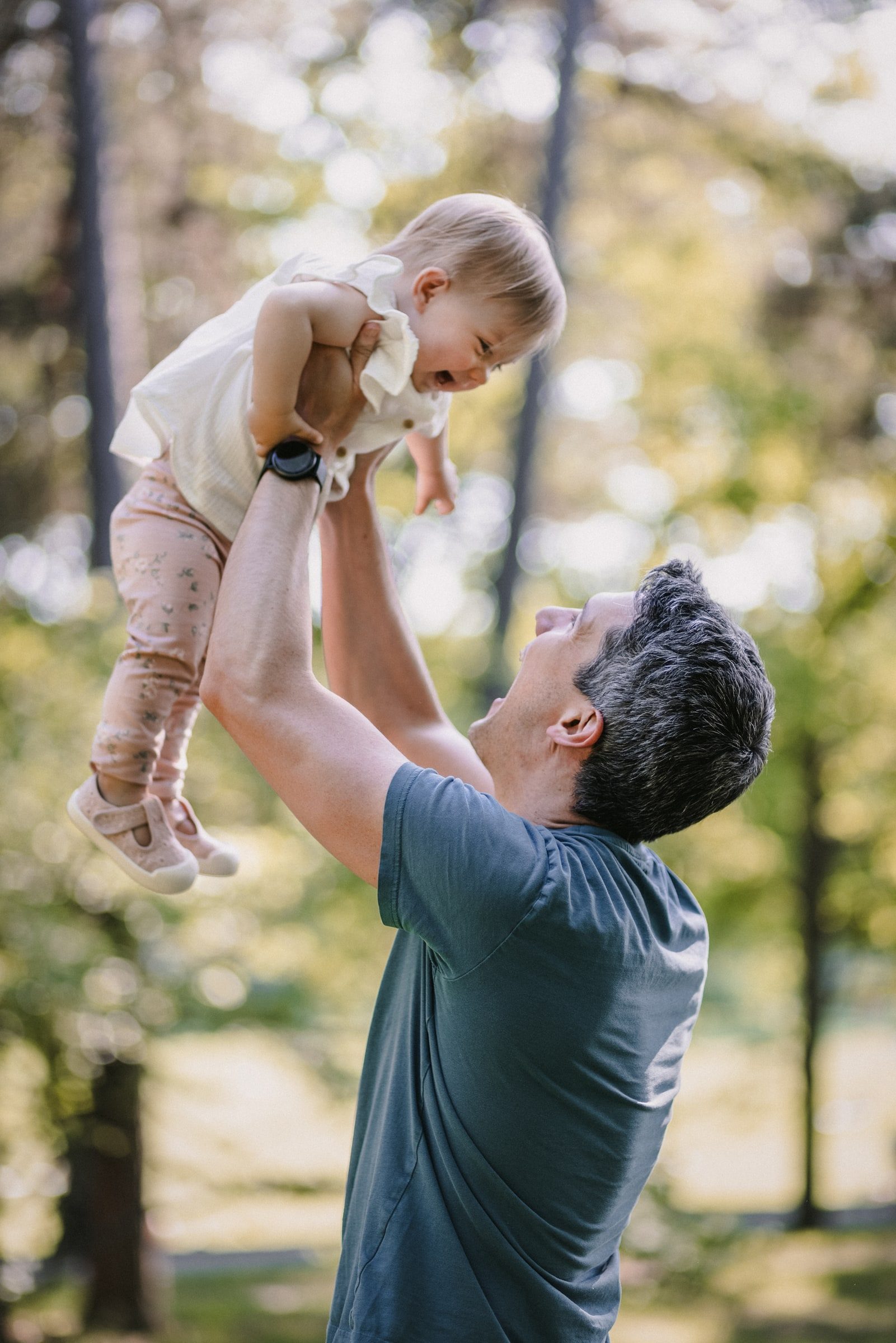 Father lifting his laughing toddler during an outdoor family session.