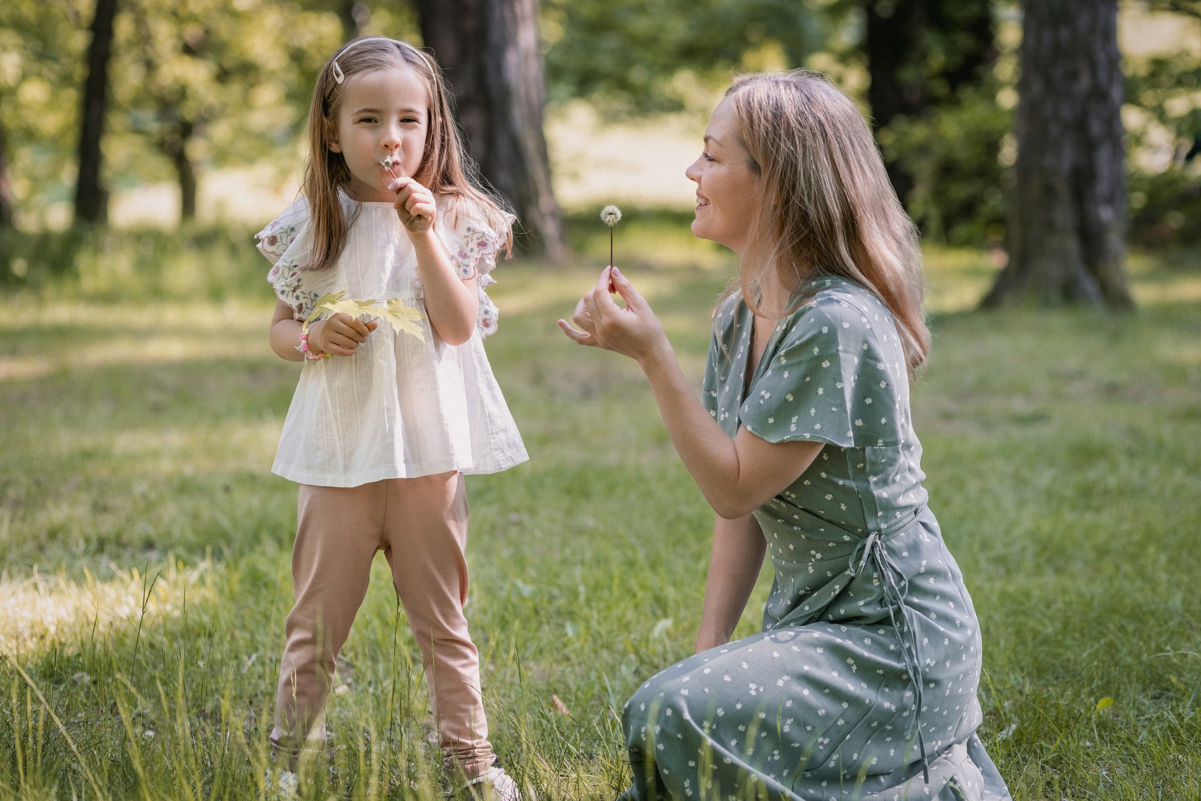 Mother and daughter playing with dandelion seeds in a summer meadow.