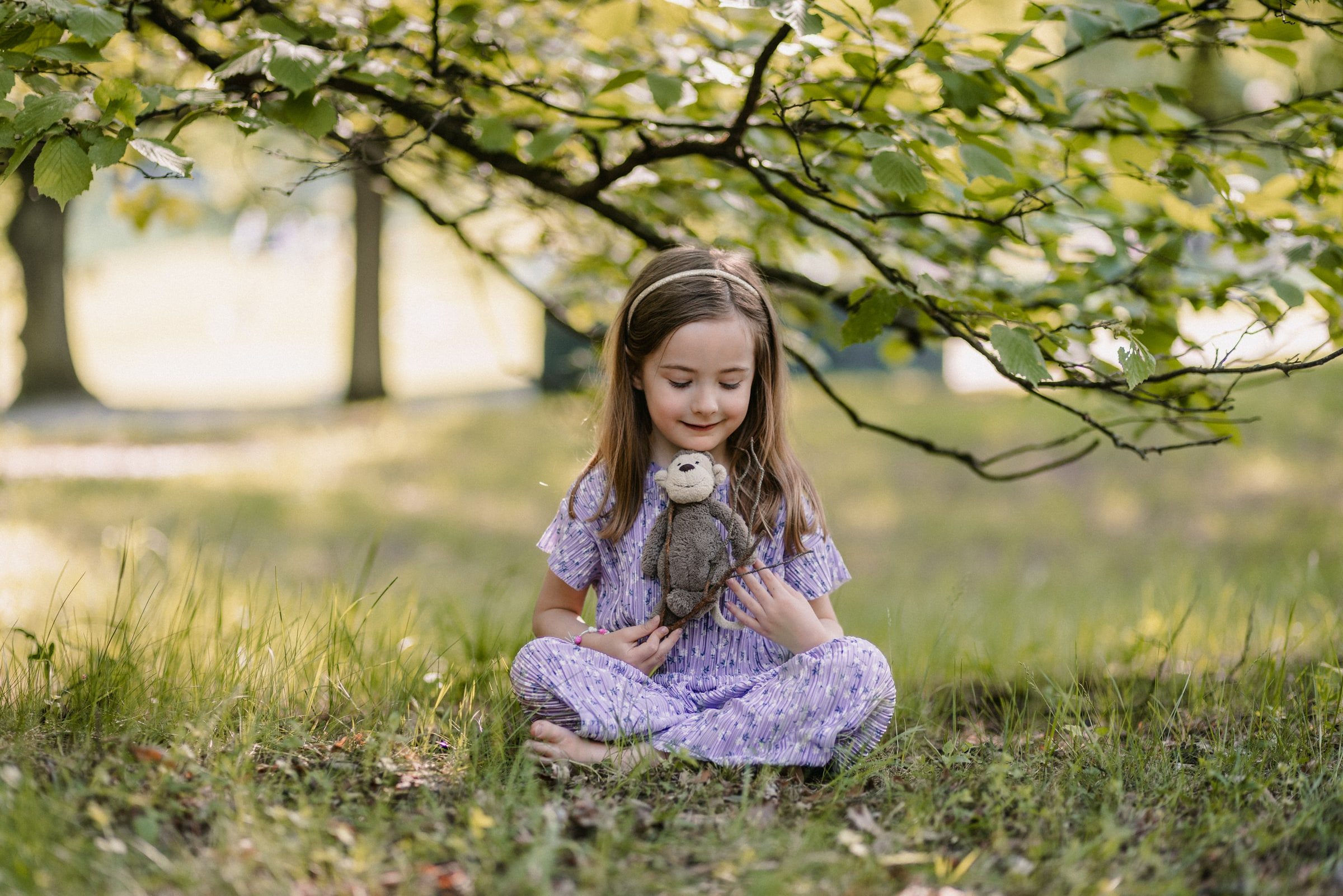 Girl in a purple dress sitting quietly beneath a leafy tree.