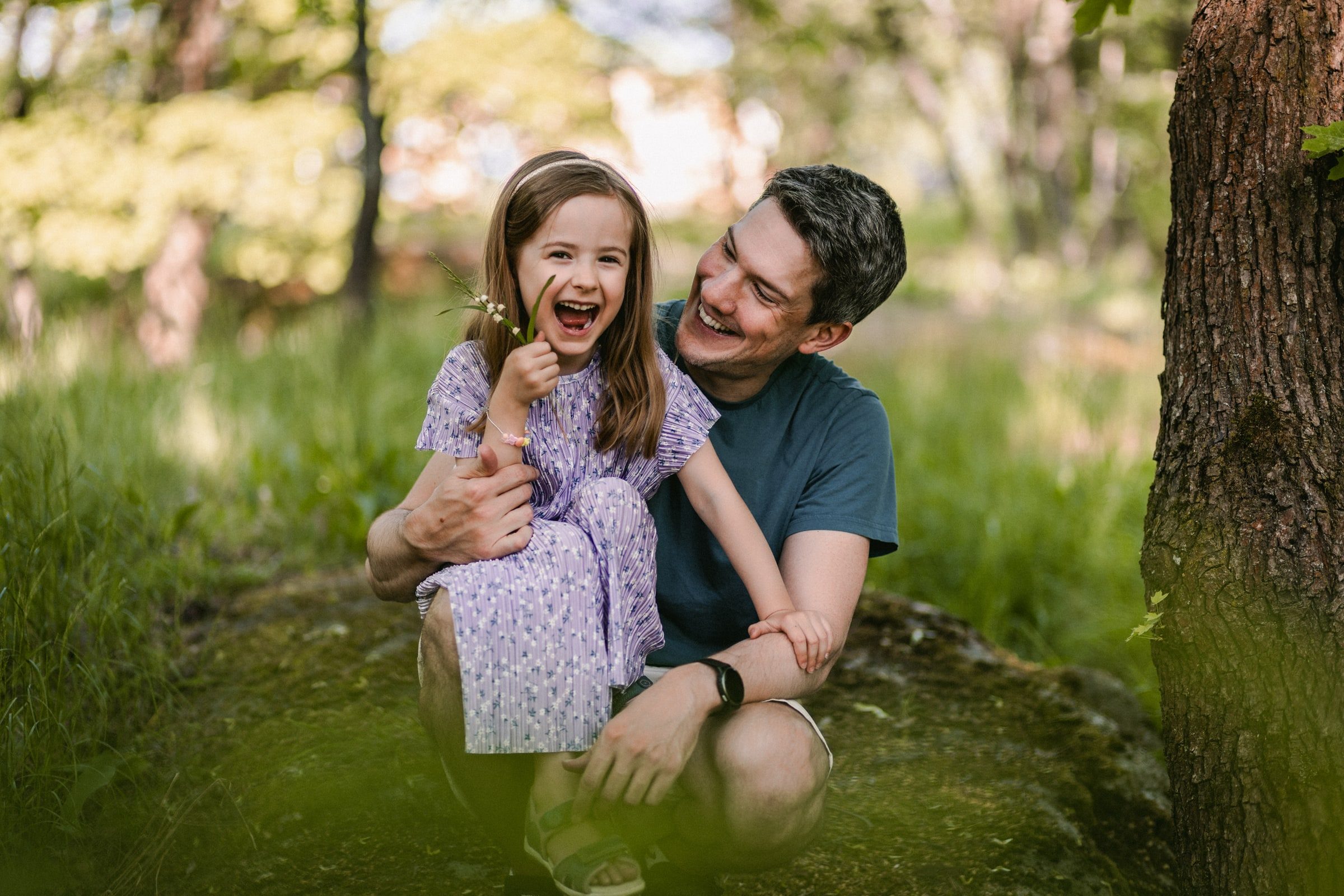 Father and daughter laughing together on the grass in warm evening light.