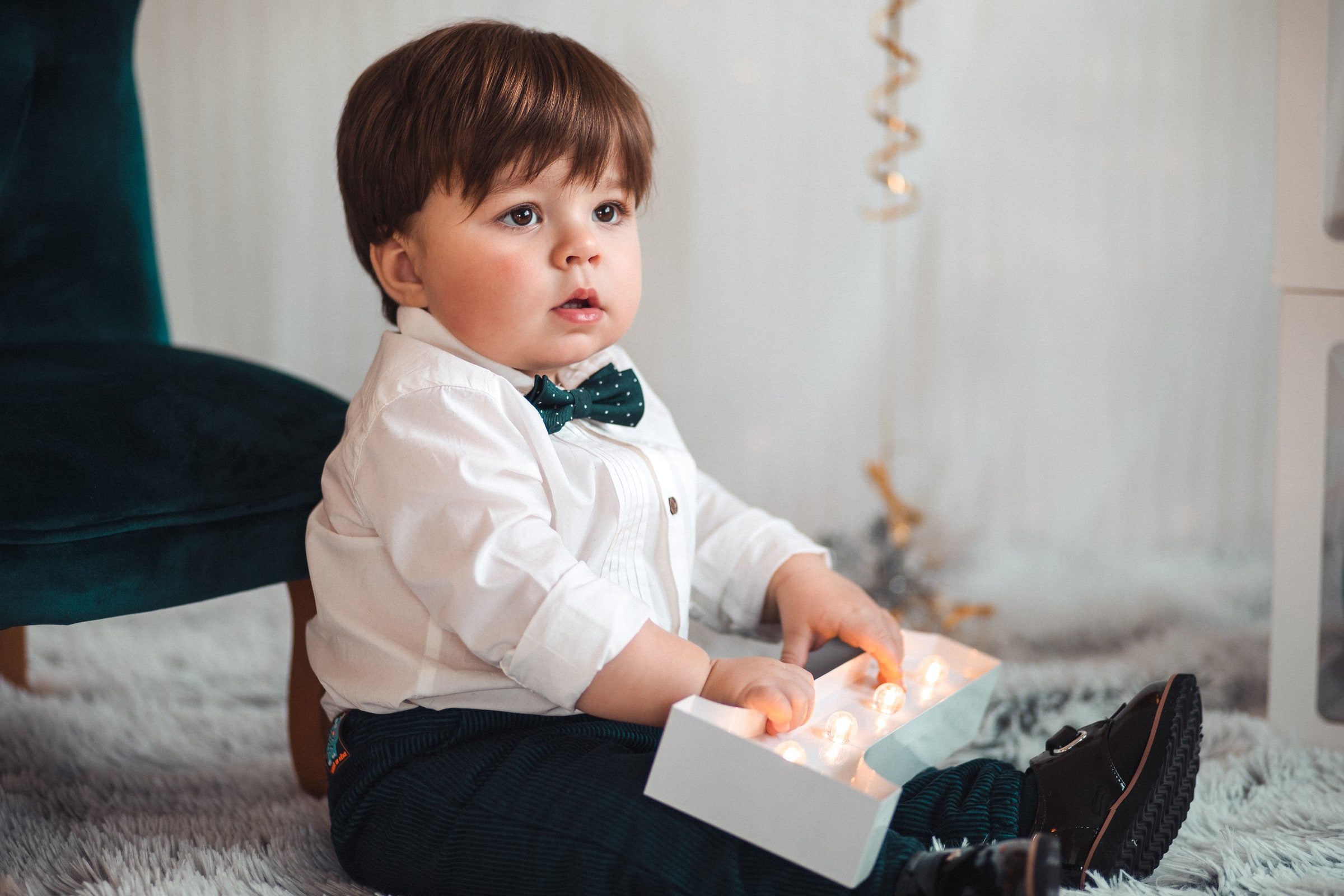 Close first-birthday portrait of a baby in a white shirt and green bow tie.