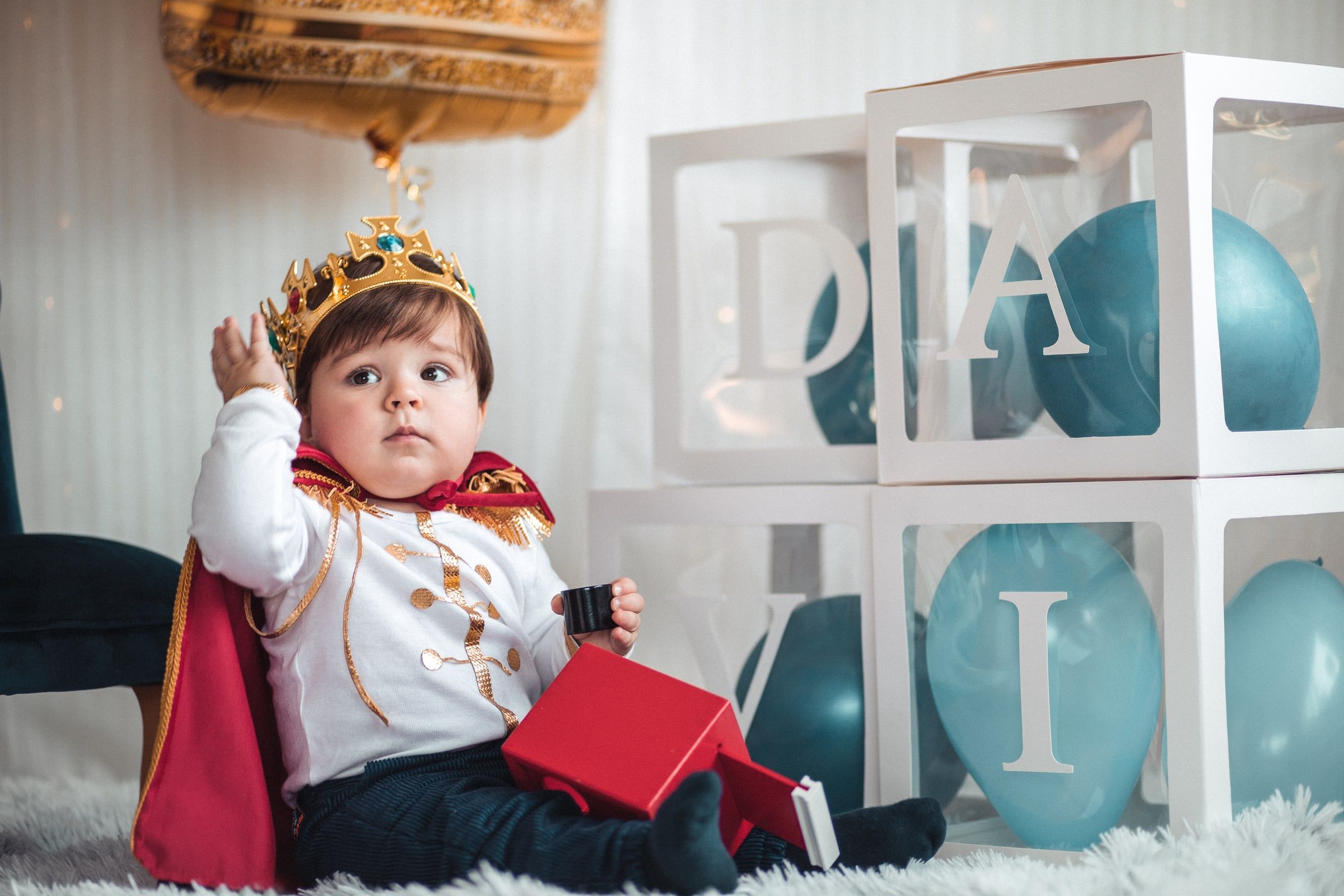 Baby wearing a small crown and holding a red gift box during the portrait session.