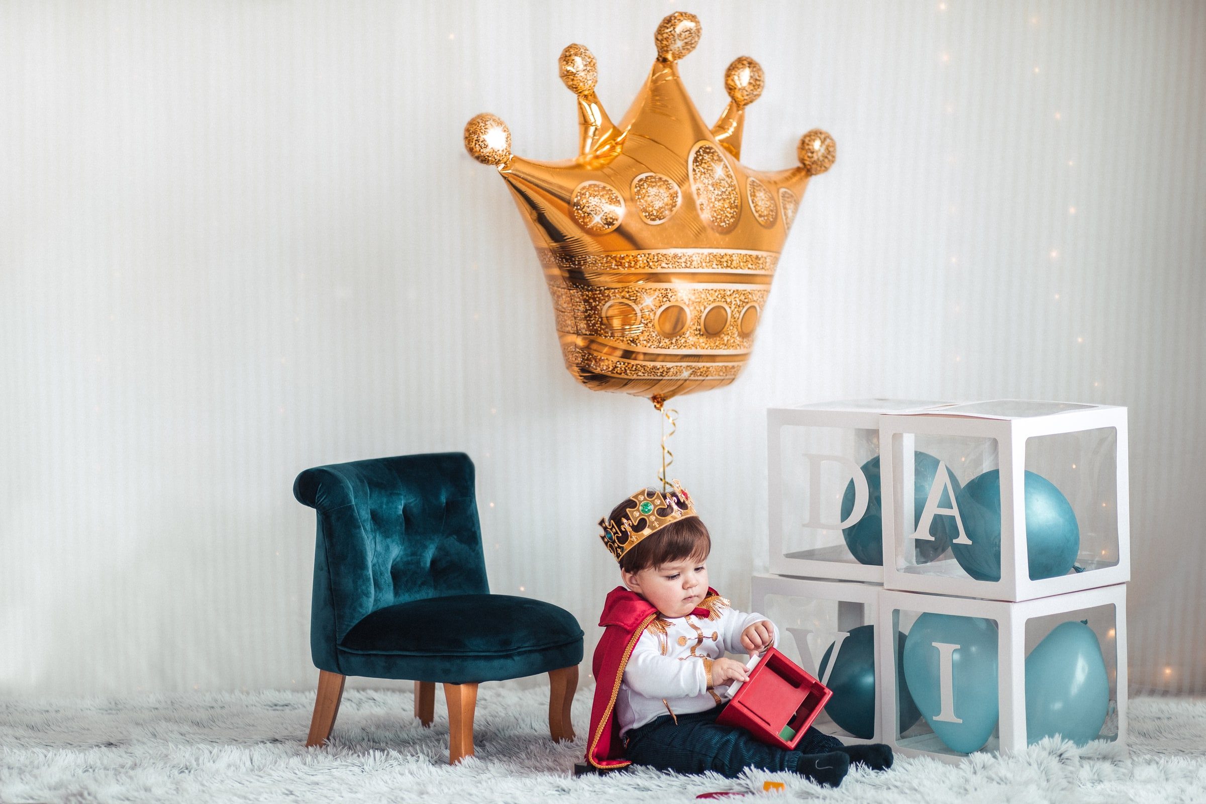 Wide portrait of the birthday child in costume beneath the gold crown balloon.