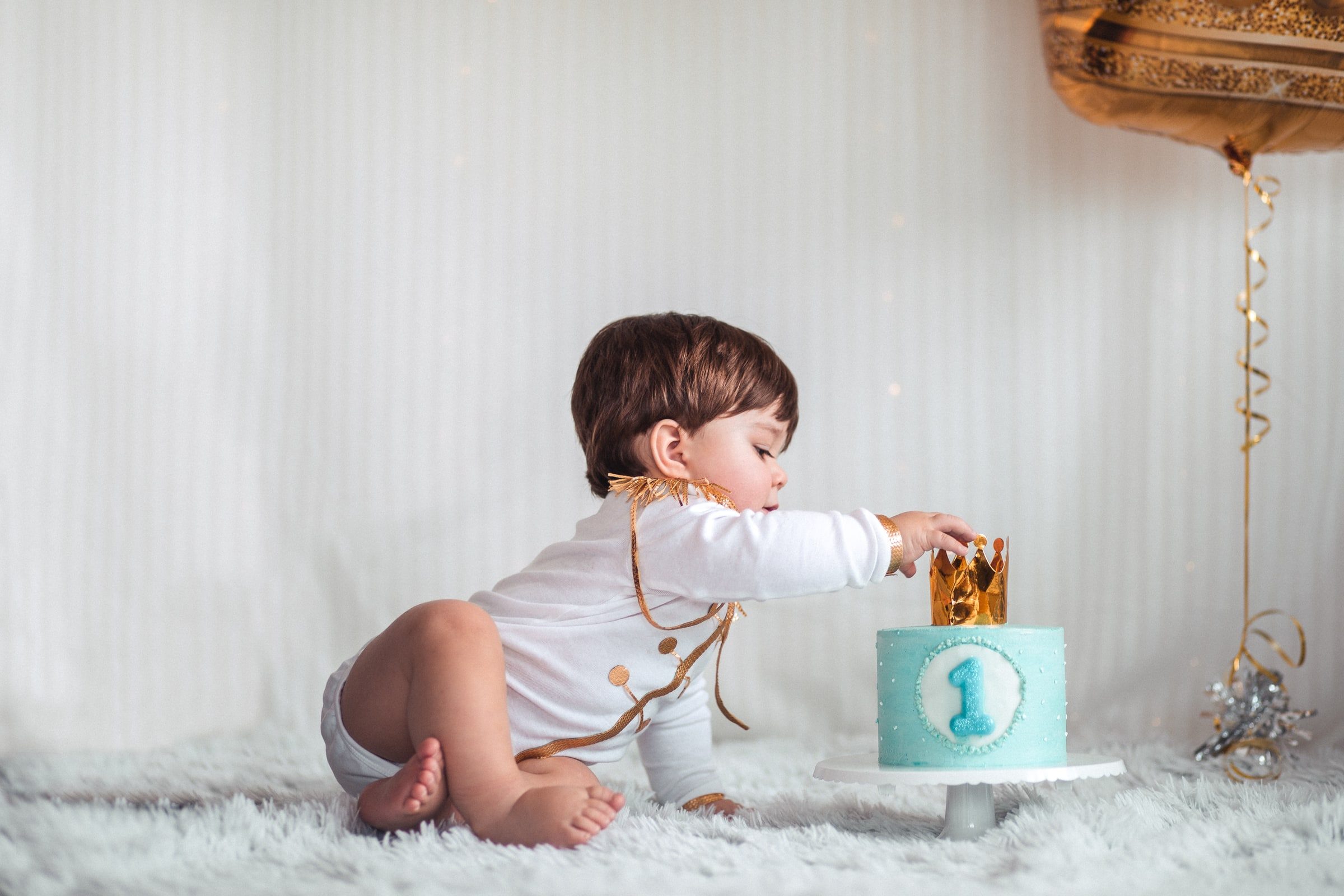 Baby reaching into a small blue first-birthday cake during the cake-smash sequence.
