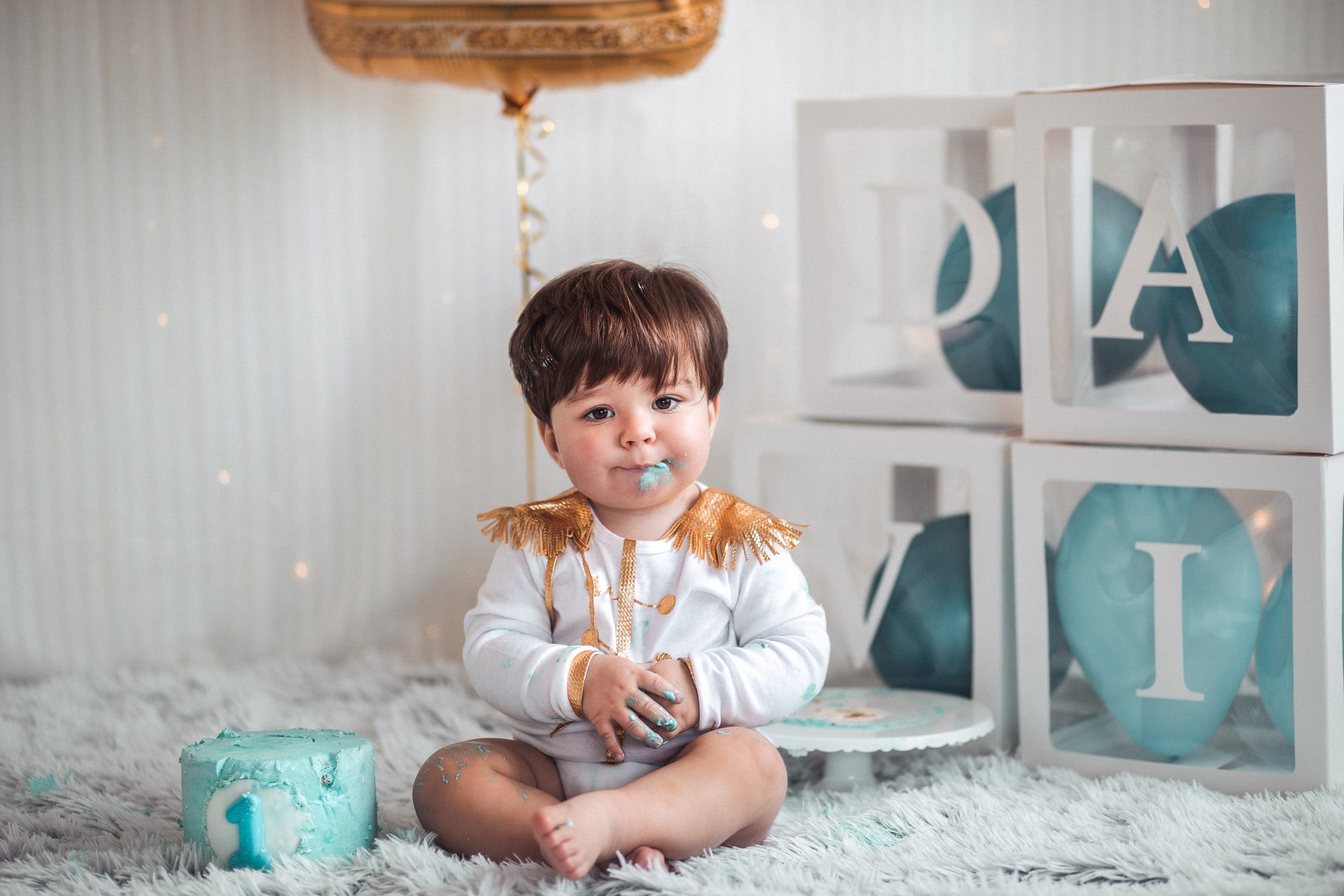Baby seated beside the birthday cake with blue icing on his face.