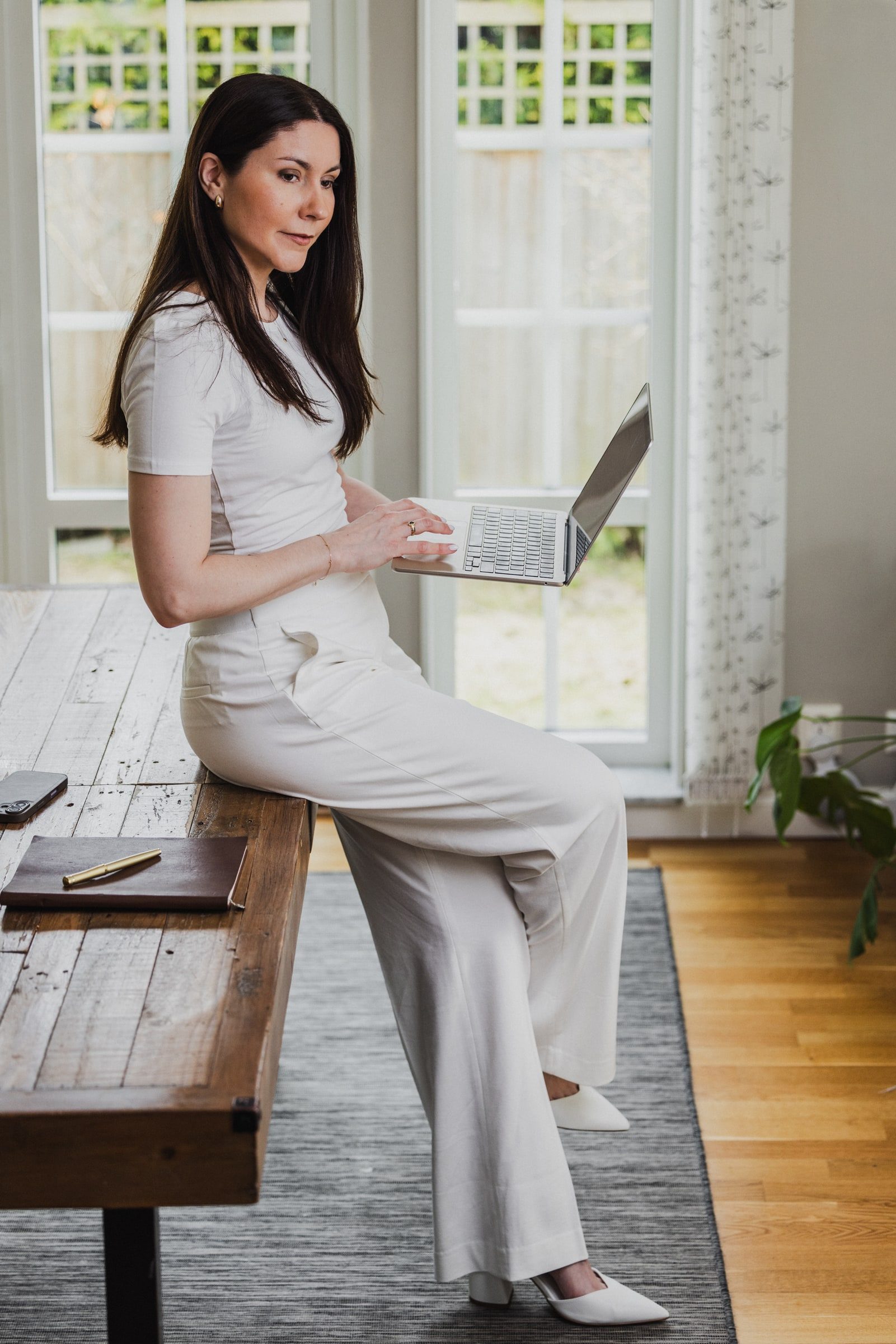 Business coach working on a laptop beside a large window.
