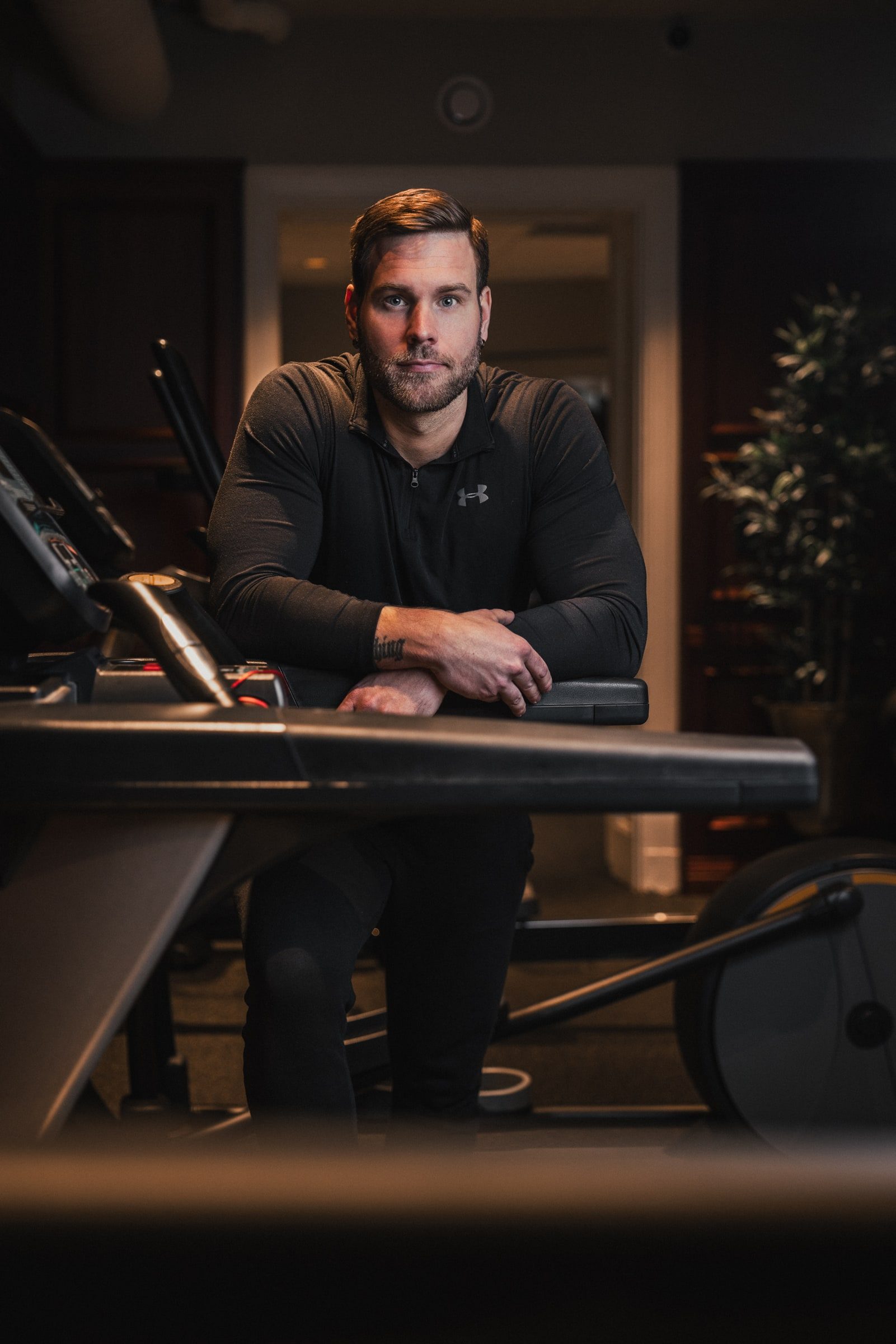 Personal trainer leaning on cardio equipment for a branding portrait.