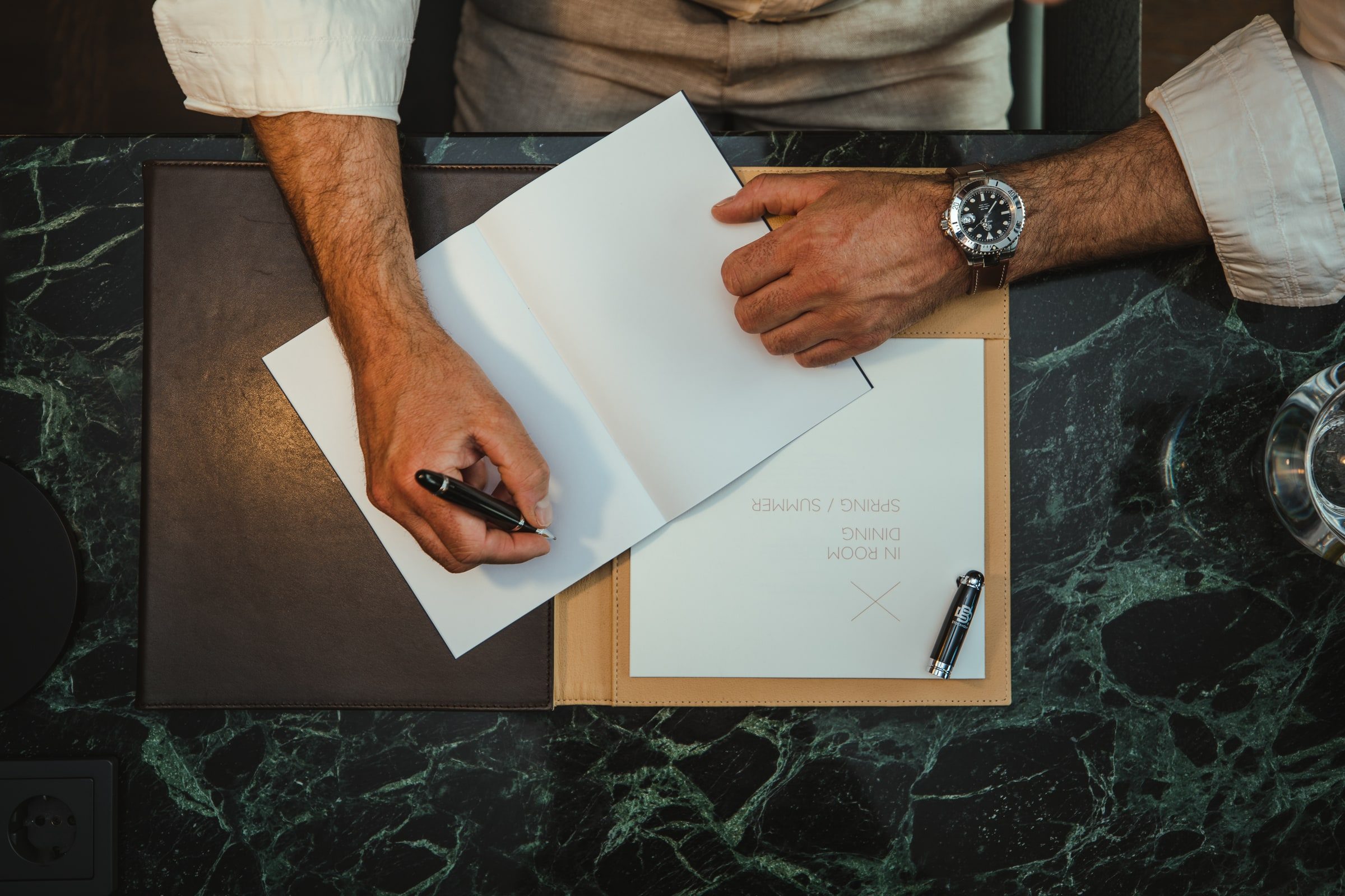 Wristwatch visible while a professional writes at a marble desk.