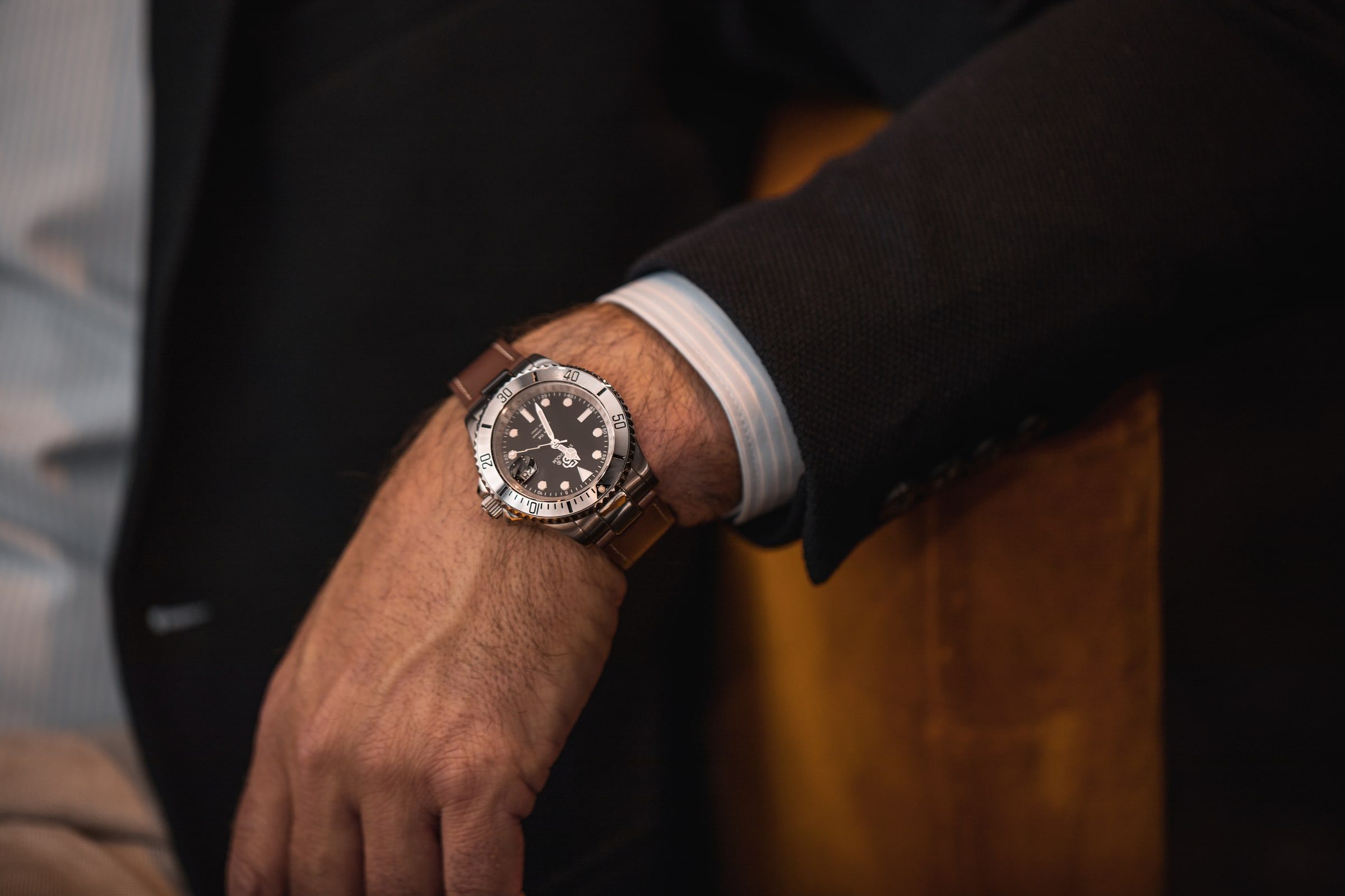 Wristwatch photographed on a tailored sleeve in a hospitality setting.