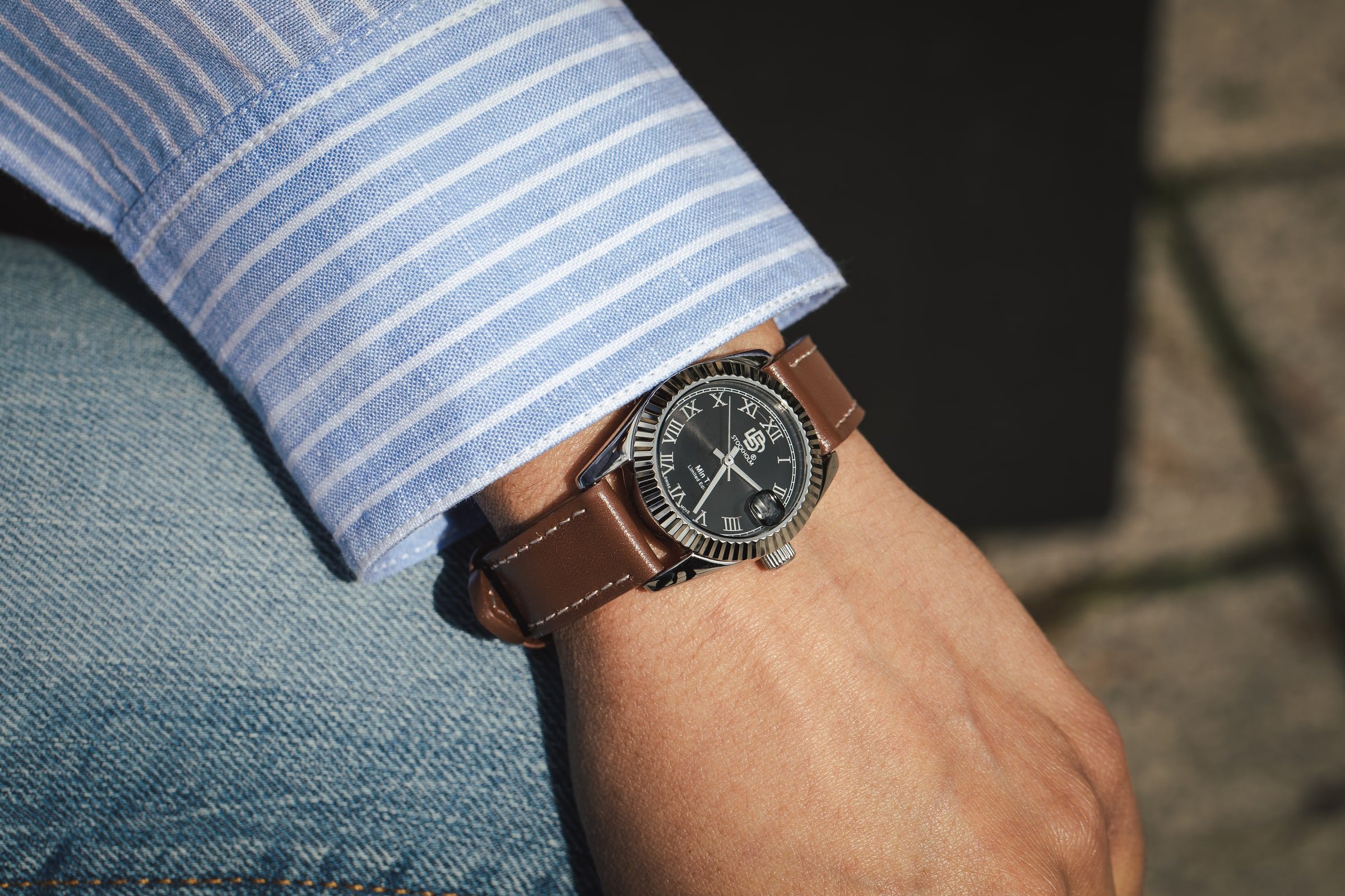 Leather-strap wristwatch photographed with a blue tailored sleeve.