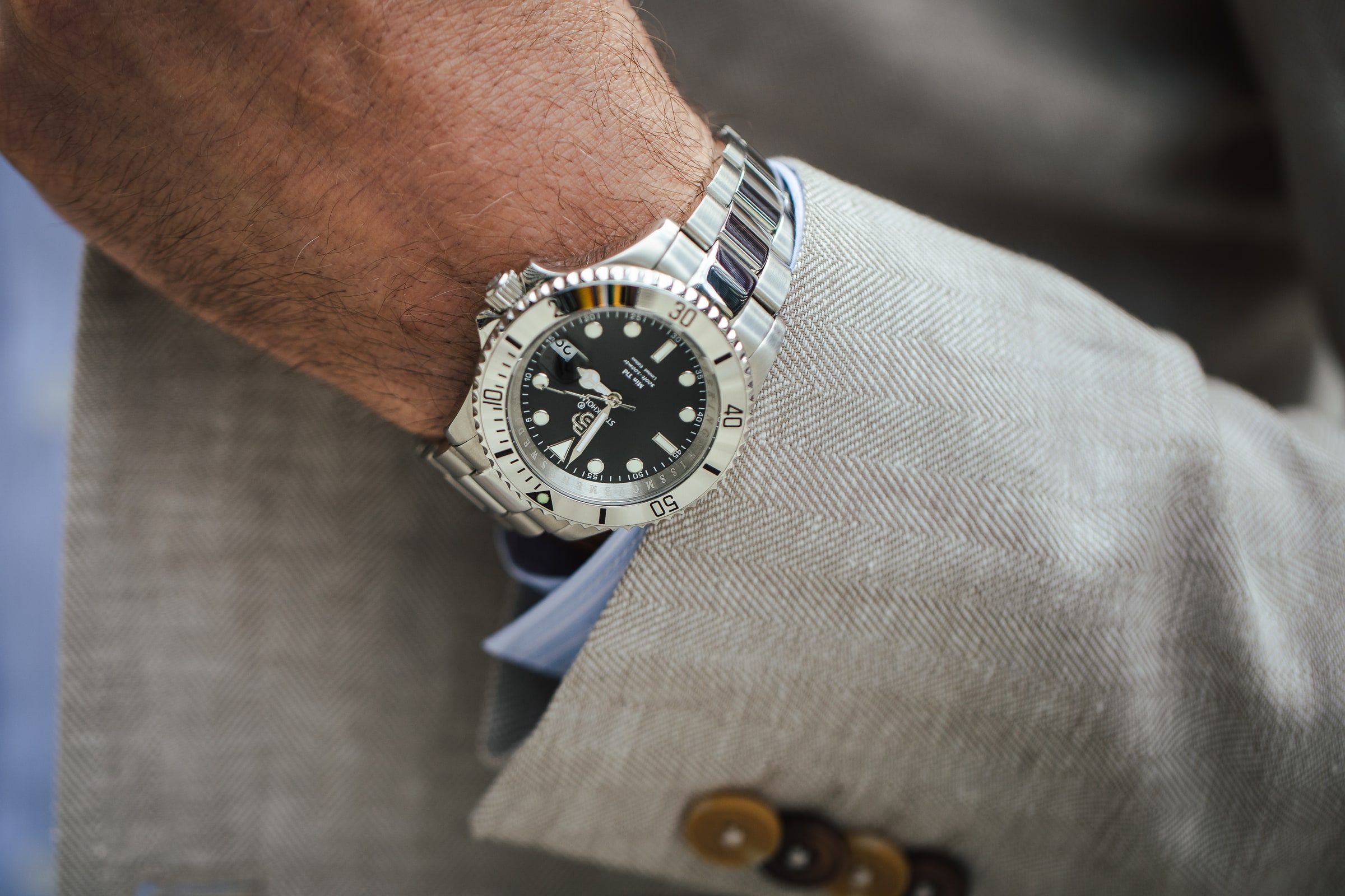 Detailed view of a steel wristwatch against textured tailoring.