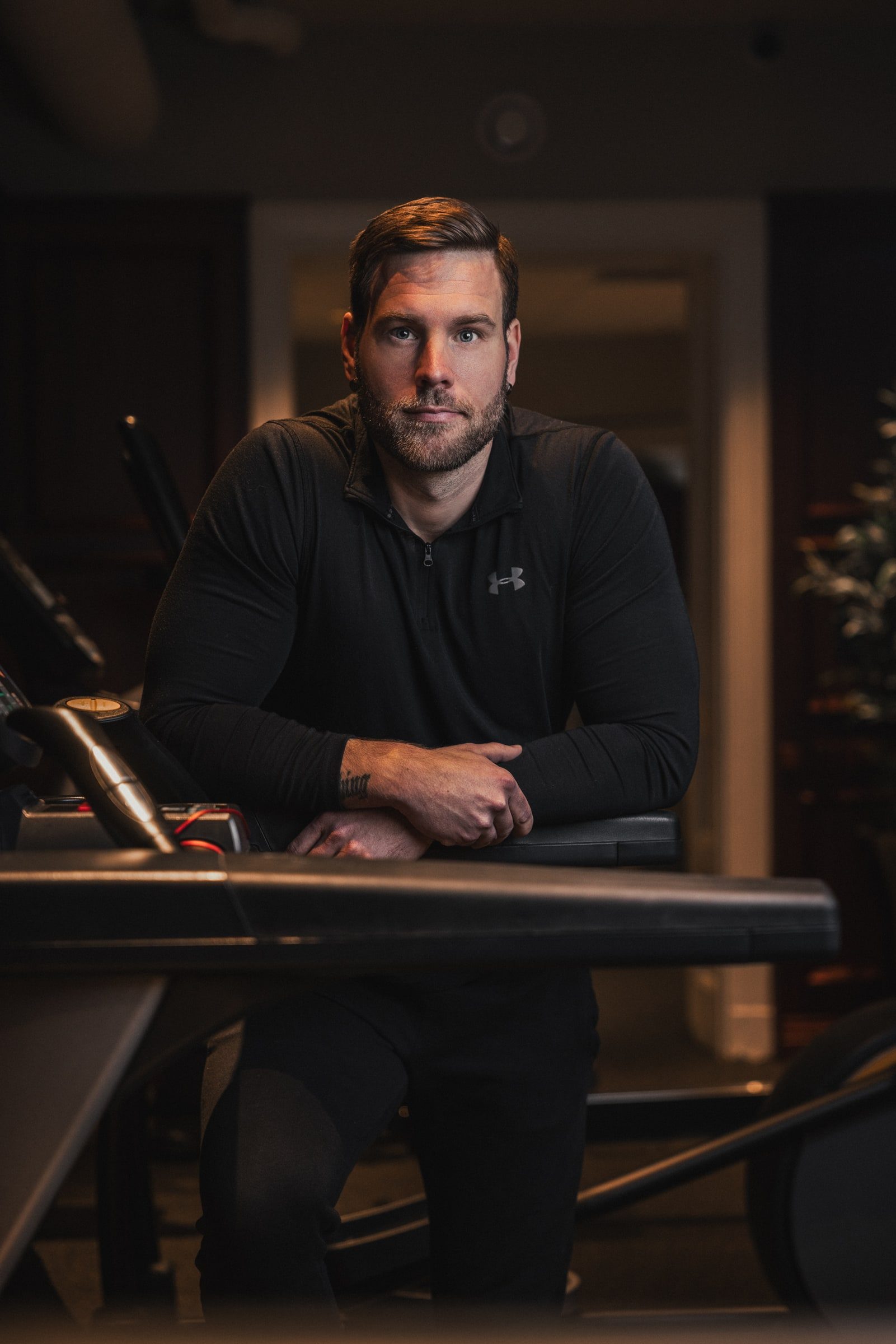 Personal trainer seated between gym equipment for a professional portrait.